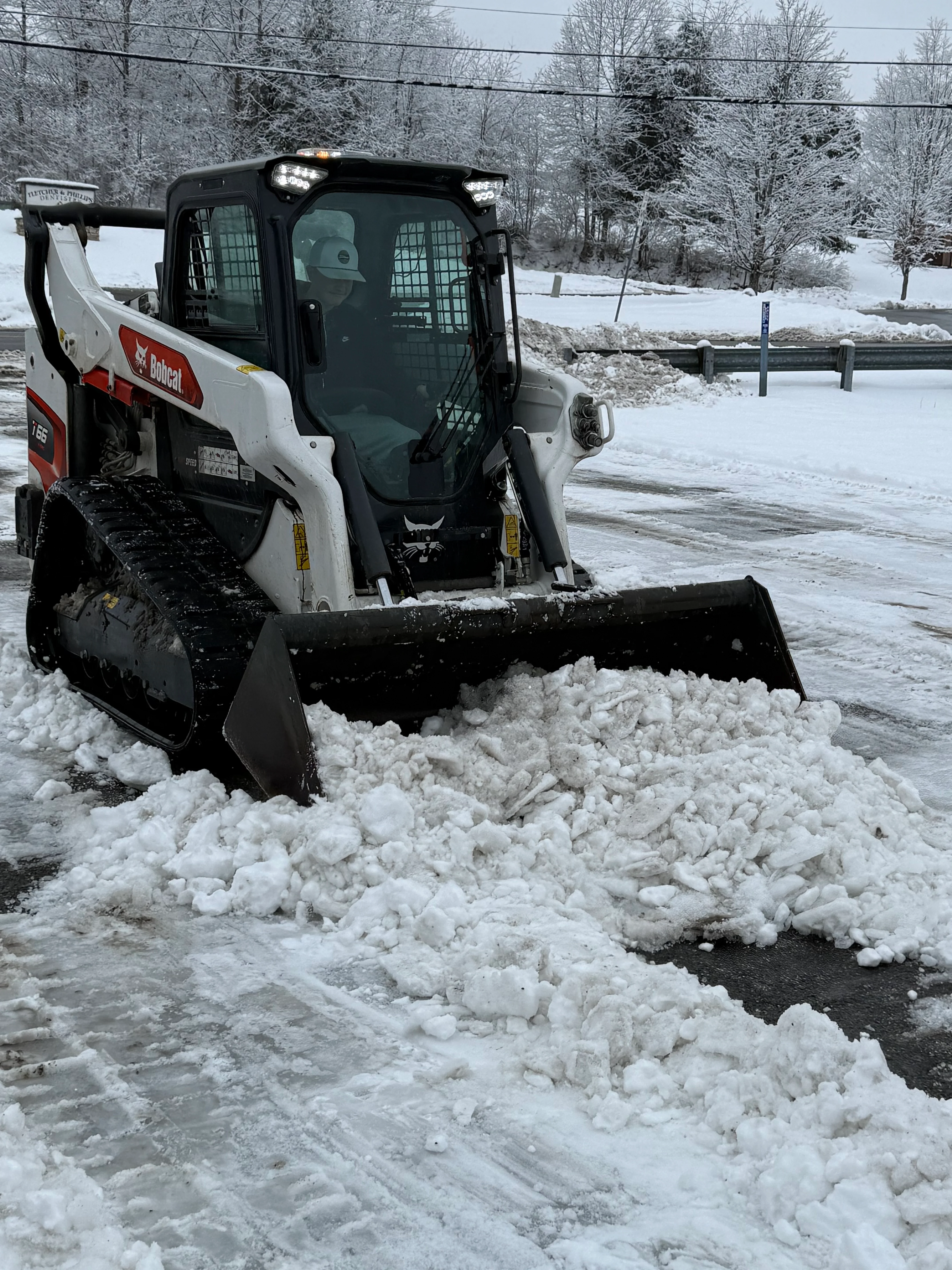 Heavy equipment clearing snow from a residential driveway during winter storm
